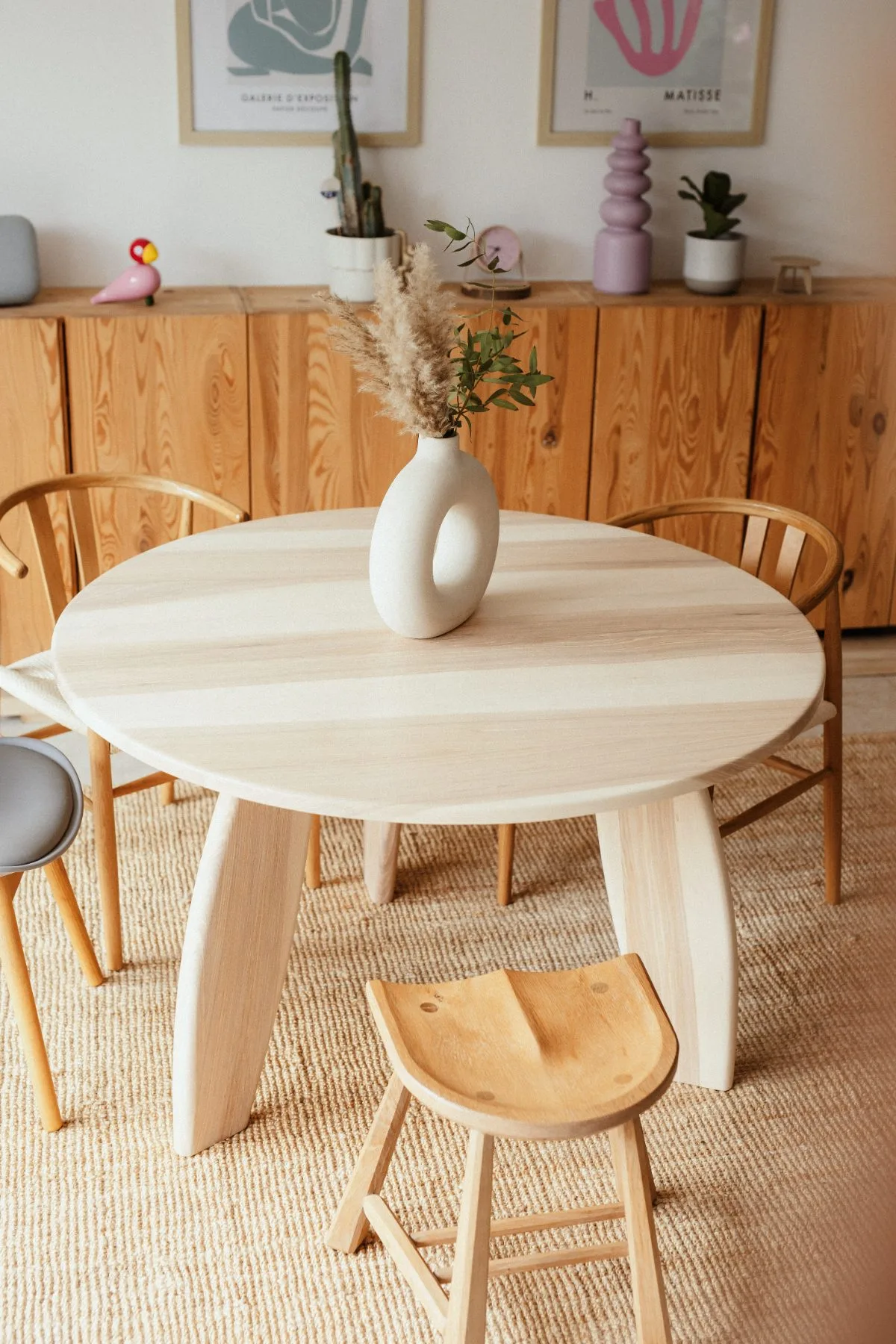 Runder Esstisch aus Esche vor einem Sideboard, darauf eine Vase mit Trockengräsern
