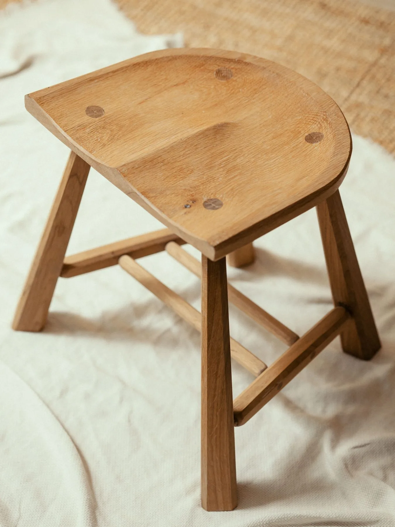 Hocker aus Eiche mit geformter Sitzfläche vor hellem Stoff